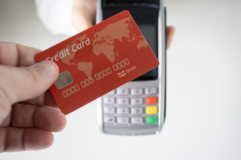 person-holding-a-red-credit-card-with-a-blurry-payment-terminal-in-the-background_181624-23860.jpg
